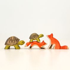 three small wooden animals sitting next to each other on a white surface with one turtle and the other tortoise