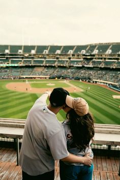 a man and woman standing next to each other in front of a baseball field