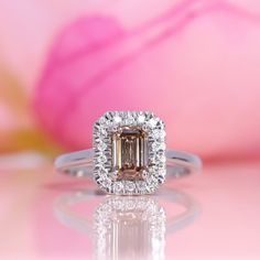 an engagement ring with a large diamond surrounded by small round brilliant cut diamonds on a pink background