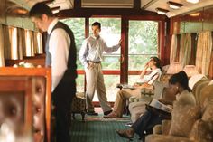 two men are standing on the inside of a train car with people sitting in seats