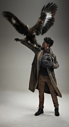 a man holding an eagle in his right hand and wearing a hat on the other