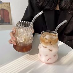 a woman sitting at a table with two drinks in front of her and another drink on the side