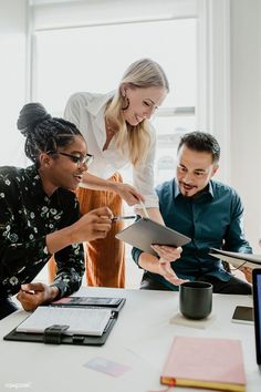 three people are gathered around a table looking at something on a clipboard in front of them