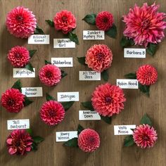 a bunch of pink flowers with name tags attached to them on a wooden table top