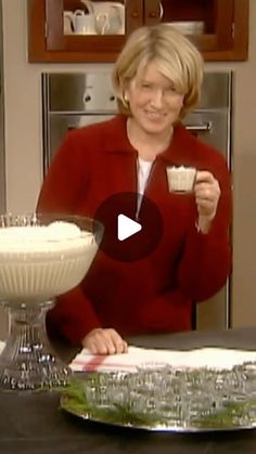 a woman holding a cup and spoon in her hand while sitting at a kitchen table