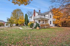 a large white house sitting on top of a lush green field covered in fall leaves