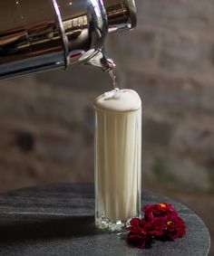 a glass filled with liquid next to a red flower