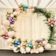 a wreath made out of balloons and greenery is displayed on a stage with white drapes