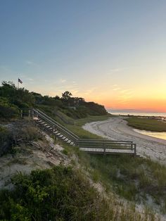 the sun is setting at the beach and there are benches on the sand