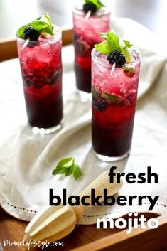 three glasses filled with ice and berries on top of a wooden tray next to a spoon