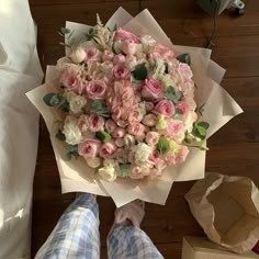 a bouquet of pink and white flowers sitting on top of a table next to someone's feet