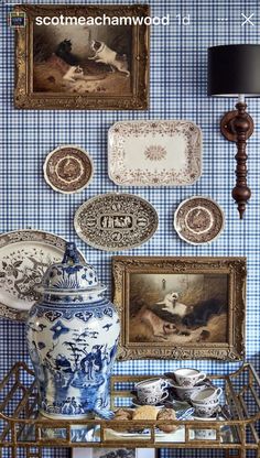 blue and white china on display in front of two framed pictures, one with an antique urn