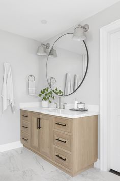 a bathroom with a large round mirror above the sink and wooden cabinetry on the side