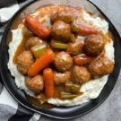 meatballs and carrots on mashed potatoes with gravy in a black plate