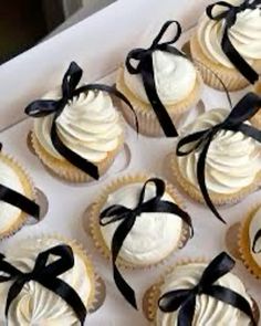 twelve cupcakes with white frosting and black ribbon tied around the edges in a box