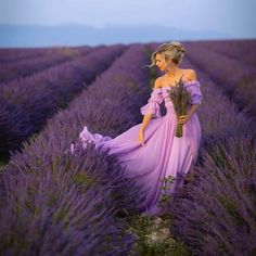 a woman in a lavender field wearing a long purple dress and holding a bunch of flowers