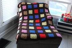 a crocheted blanket sitting on top of a couch in front of a window