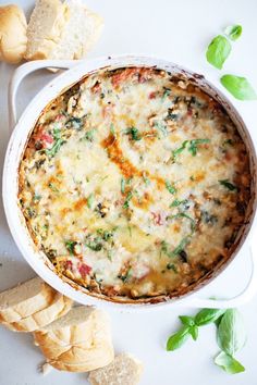 a casserole dish with spinach, cheese and bread next to it on a white surface