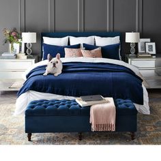 a blue bed with white sheets and pillows in a gray room next to two nightstands