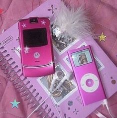 two pink cell phones sitting next to each other on top of a notebook with ear buds