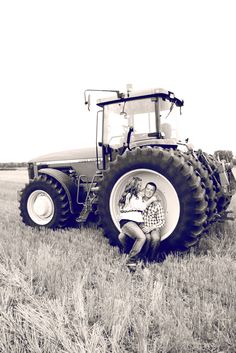 a man and woman sitting in front of a large tractor on a field with grass