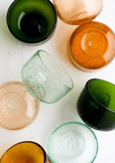 several different colored glass cups sitting on top of a white countertop next to each other