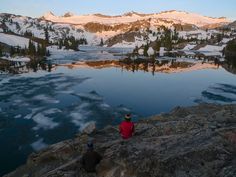 two people sitting on rocks looking out at the mountains and lake in the distance,