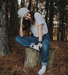 a young woman sitting on top of a tree stump in the middle of a forest