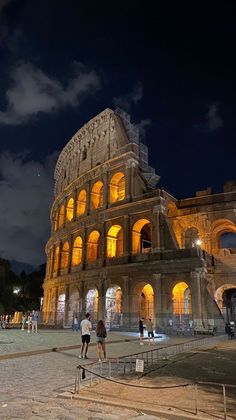 the colossion is lit up at night with people walking around in front of it