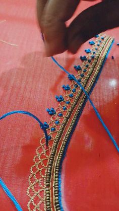 someone is working on a piece of cloth with blue thread and gold trimmings