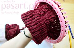 a hand holding a red knitted hat on top of a wooden table next to yarn