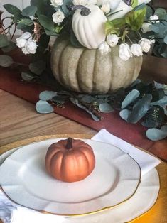 a pumpkin sitting on top of a white plate next to a vase filled with flowers