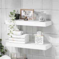 two white shelves with towels and other items on them in a bathroom, next to a potted plant