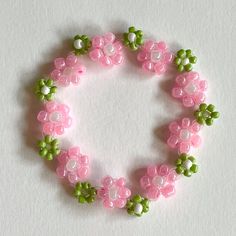 a pink and green beaded bracelet with flowers on it's end, sitting on a white surface