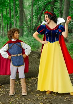 a young boy standing next to a woman dressed as snow white in the woods with an apple