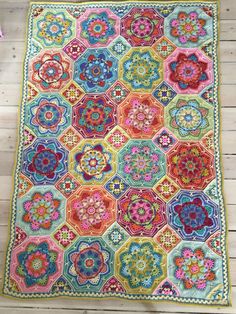 a multicolored quilt is laying on a wooden floor next to a pink flower arrangement