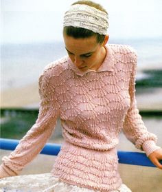 a woman in a pink sweater and white skirt is leaning against a rail with her hands on her hips