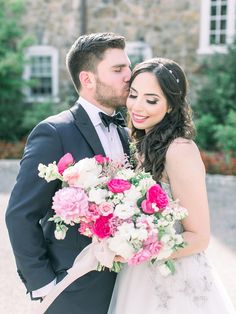 a bride and groom kissing in front of a stone building with pink and white flowers