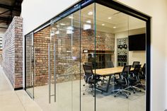 an empty conference room with glass walls and brick wall in the background, along with black chairs around a wooden table