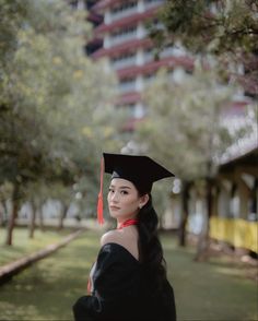 a woman wearing a graduation cap and gown standing in front of a building with trees