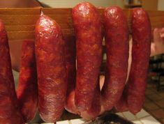 several sausages are hanging from a rack in a kitchen with people looking at them