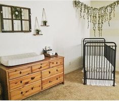 a baby crib and dresser in a room with plants hanging on the wall above it