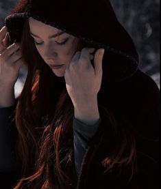 a woman with red hair wearing a black coat and holding her hands to her ear