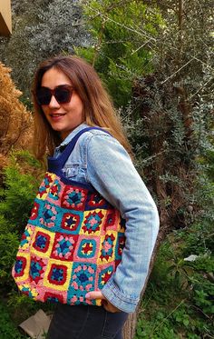 a woman wearing sunglasses and carrying a multicolored crocheted bag