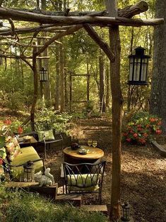 an outdoor seating area in the woods with lots of plants and flowers around it,