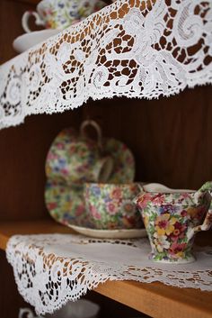 there are lace doily on the shelf above tea cups and saucers in this room