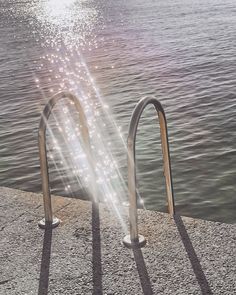 the sun shines brightly behind two metal railings by the water's edge