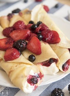 crepes filled with berries and cream on a white plate next to blackberries