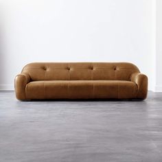 a brown leather couch sitting on top of a cement floor next to a white wall