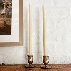 two candles sitting on top of a wooden table next to a framed photo and painting